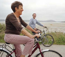 old couple riding bikes along the beach 